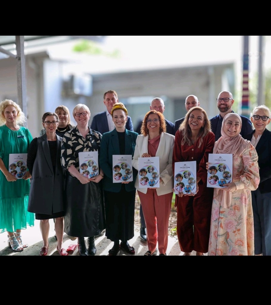 A group of smiling people hold up copies of the Early Years Strategy.
